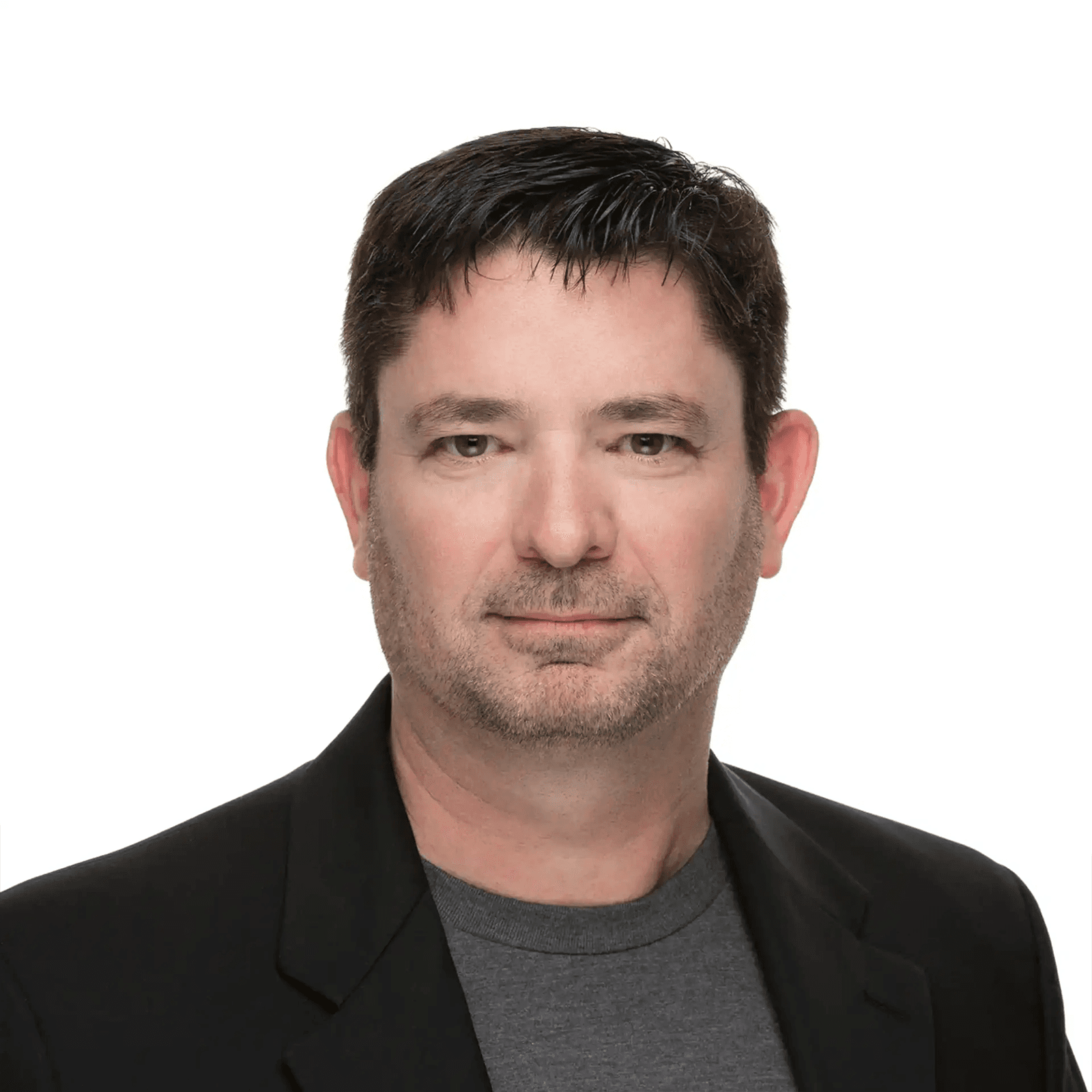 Headshot of a man with dark hair and stubble, wearing a dark jacket over a grey t-shirt, against a white background.