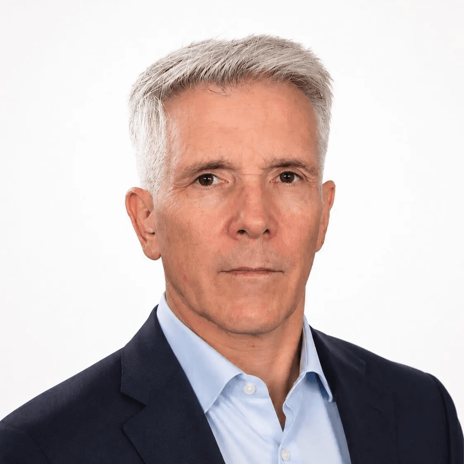A man with gray hair and a serious expression, wearing a navy suit and light blue shirt, looks straight ahead.